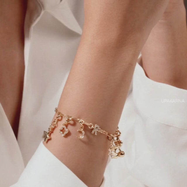 Close-up video of a gold-tone charm bracelet worn on the wrist, featuring multiple dangling charms including bows, hearts, stars, crescent shapes, and crystal accents.