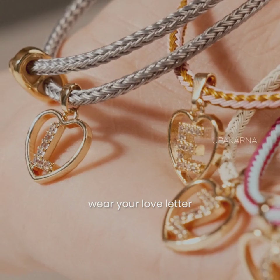 Alt text: Close-up of hands customizing a white woven bracelet with gold-tone letter charms, showcasing a personalized DIY bracelet from Upakarna.