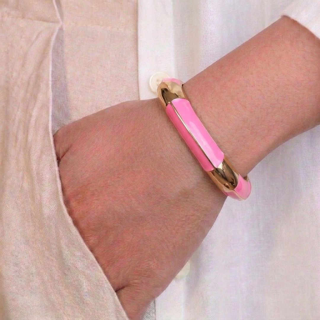 Luxury gold anti-tarnish bangle featuring glossy pink enamel panels, a bold geometric silhouette, and polished stainless steel construction, elegantly worn on the wrist with a white linen outfit