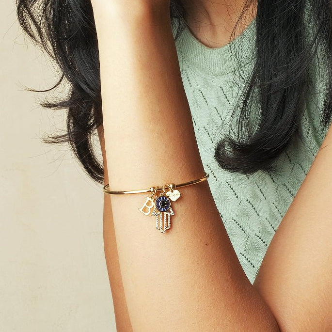 Elegant personalized Hamsa bracelet with an initial charm, heart charm, and evil eye detailing, crafted with an anti-tarnish finish for everyday wear, meaningful gifting, and lasting style.
