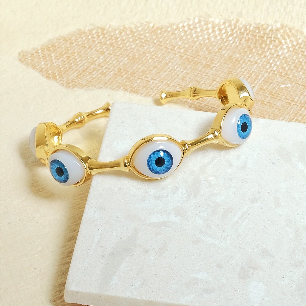 Elegant golden evil eye bangle with multiple charm detailing and an adjustable anti-tarnish finish, perfect for everyday styling, protective charm looks, and chic stacked wear.
